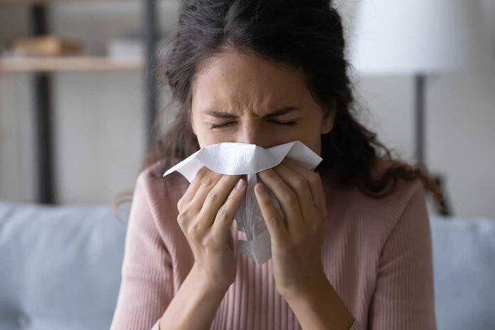 1906128409 Woman sneezing into a tissue indoors