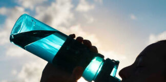 Silhouette of person drinking from a water bottle.
