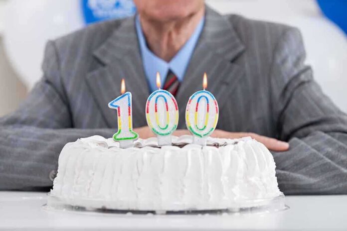 shutterstock_161175410.jpg A man in a suit sitting in front of a birthday cake with 100 candles