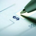 Close up of a pen poised over a check with a dollar sign