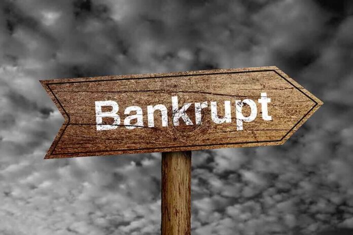 shutterstock_243618139.jpg Wooden arrow sign pointing towards the word Bankrupt against a cloudy background