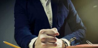 A mans clenched fist resting on a desk with office supplies nearby