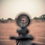 Cartel HUNTS Americans – NEW Highway TERROR Unleashed Rifle scope aimed at a distant target outdoors.