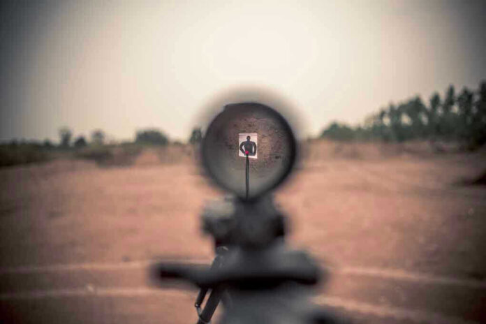 Rifle scope aimed at a distant target outdoors.