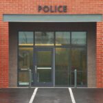 Surveillance SCANDAL—Top Cop Falls in Hours Entrance of a modern police station with brick facade