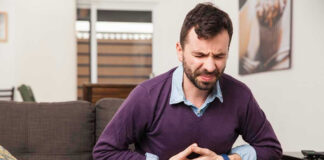 Man sitting on couch, holding stomach in pain.