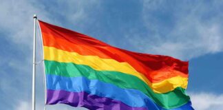 A rainbow flag waving against a blue sky