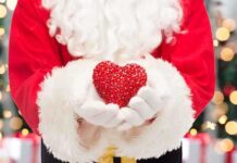 Santa Claus holding a red heart in front of a festive background