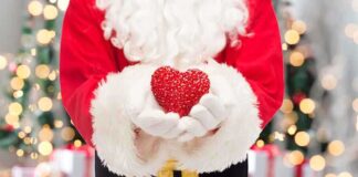 Santa Claus holding a red heart in front of a festive background