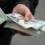 Elite Families Aid Foreign Telecom Takeover A hand holding a stack of hundred dollar bills with one bill prominently displayed