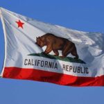 Trump’s $10 Billion Freeze SHOCKS California California state flag featuring a bear and a red star against a blue sky
