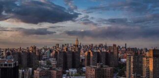 A panoramic view of New York City skyline during sunset with clouds