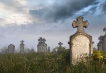 Foggy graveyard with tombstones and crosses under a cloudy sky