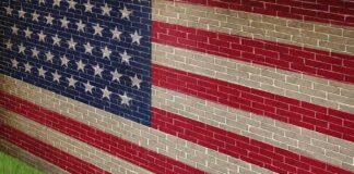 A man in a suit standing in front of a large American flag painted on a wall