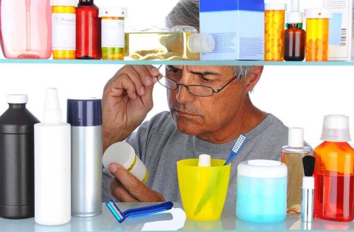 shutterstock_84519838.jpg Senior man looking closely at a product in a medicine cabinet filled with various bottles and containers