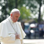 Man in white religious attire looking down thoughtfully.