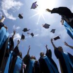Graduating students celebrating by throwing their caps into the air under a bright blue sky