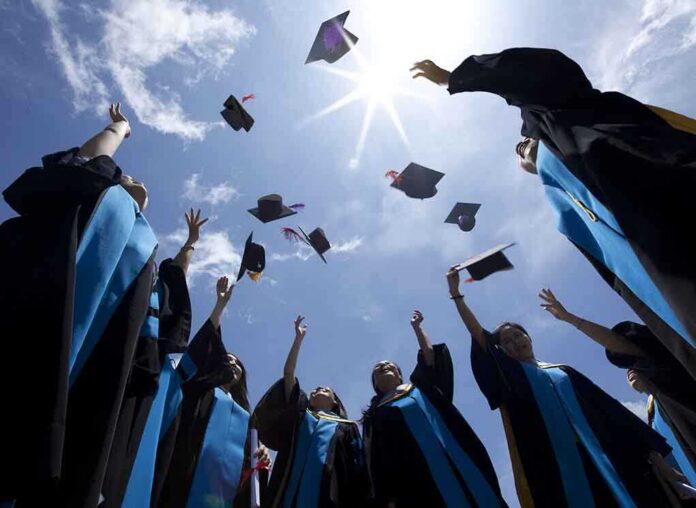 Graduating students celebrating by throwing their caps into the air under a bright blue sky