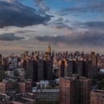 A panoramic view of New York City skyline during sunset with clouds