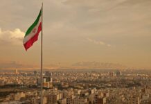 Iranian flag waving over a city skyline with mountains in the background