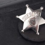 A silver sheriff badge resting on a black leather surface