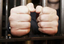 Hands gripping jail cell bars tightly.