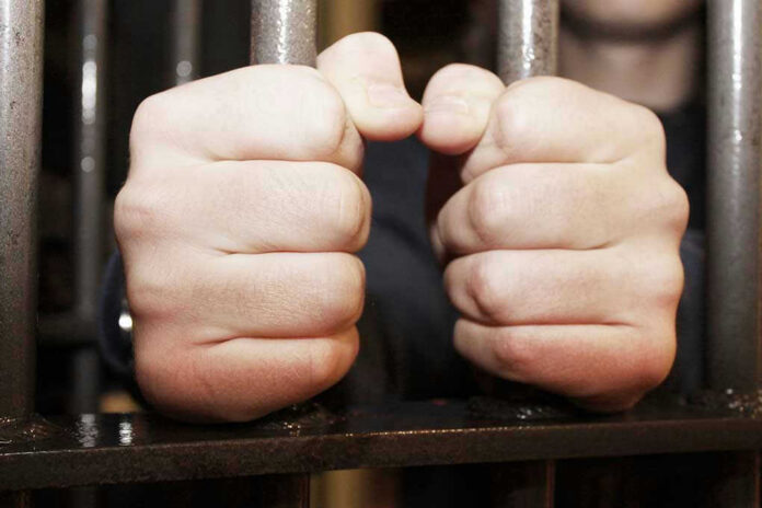 108342344 Hands gripping jail cell bars tightly.