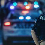 Court Slaps Cops: Guns ≠ Crime Police officer with patrol car and flashing lights.