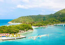 Tropical beach with docks and lush green hills.