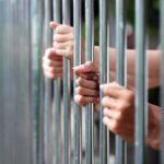 Hidden Prison Release List Sparks Uproar Hands gripping metal prison bars