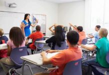 Demographic Whiplash Hits Public Schools Teacher in a blue dress instructing students in a classroom with hands raised