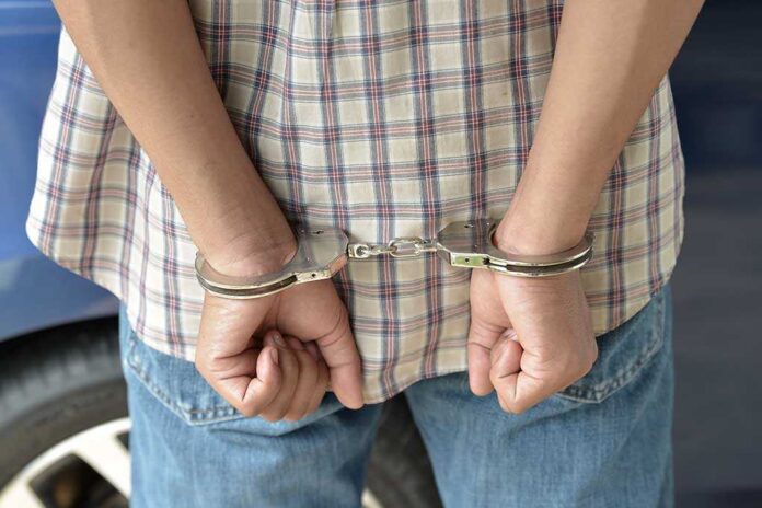 A person in handcuffs viewed from behind, wearing a plaid shirt and denim jeans