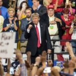 politician on stage at a rally raising a fist amid cheering crowd