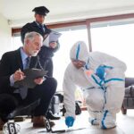 forensic investigator in protective suit collects evidence while colleagues take notes