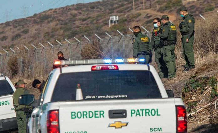 shutterstock_1900868446 Border Patrol agents gather near fence with patrol trucks