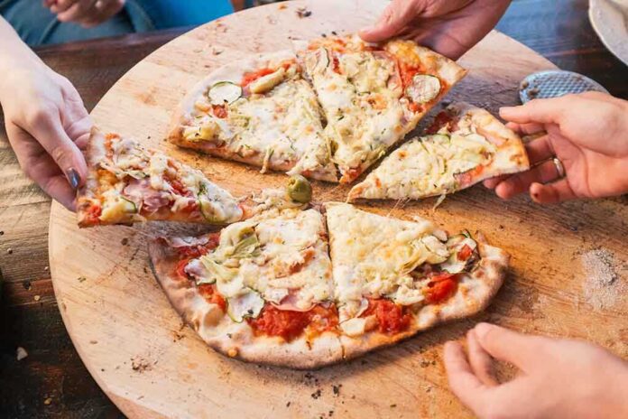 shutterstock_213558760 People sharing slices of pizza on a wooden board