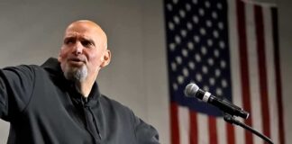 Bald man speaking at a microphone with a U.S. flag in the background