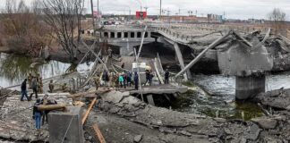 People crossing a destroyed concrete bridge over a river