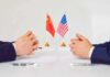 Two diplomats sit across table with China and United States flags between them
