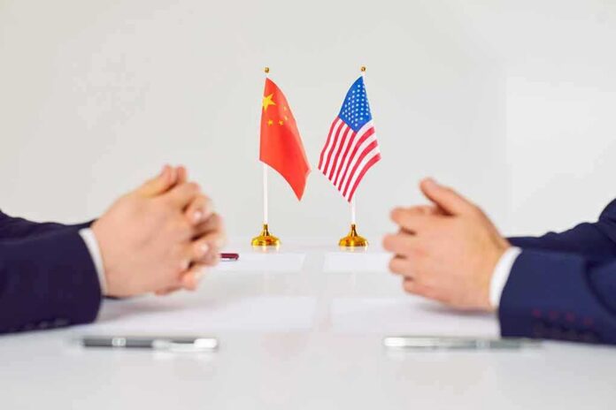 Two diplomats sit across table with China and United States flags between them