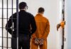 Prisoner in orange jumpsuit handcuffed and escorted by officer