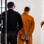 Trump Pardon Ignites ATF Firestorm Prisoner in orange jumpsuit handcuffed and escorted by officer