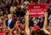 crowd at political rally holding a red sign