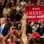 crowd at political rally holding a red sign