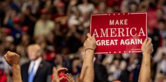 crowd at political rally holding a red sign