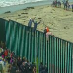 Mass Immigration RUINING Spain? People climbing a tall beachside border fence