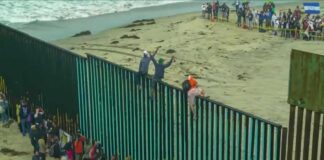 People climbing a tall beachside border fence