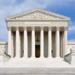 Supreme Court Showdown: Nine Forever Or Thirteen? Front view of the Supreme Court building with large columns and steps under a blue sky