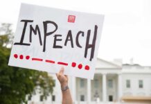 Shock Warning: Trump Targeted Immediately Protester holds an impeach sign in front of a white government building