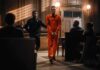 Inmate in orange jumpsuit escorted by officer in courtroom